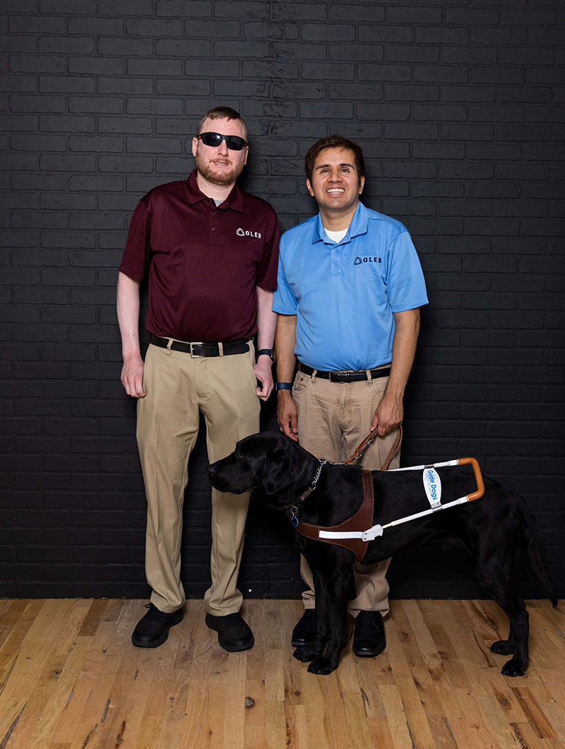 Two men stand for a picture, the man on the right is holding the leash for his guide dog