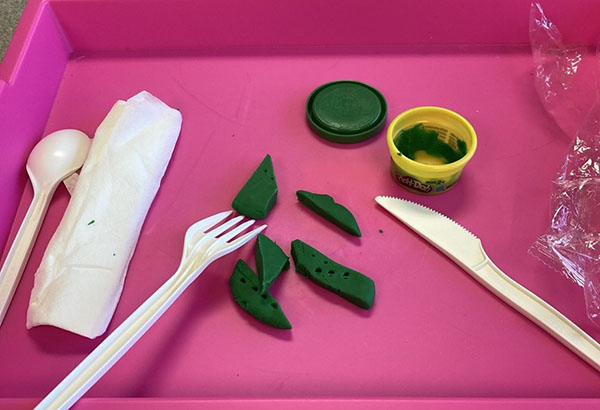 A plastic fork and knife used to cut green playdough.