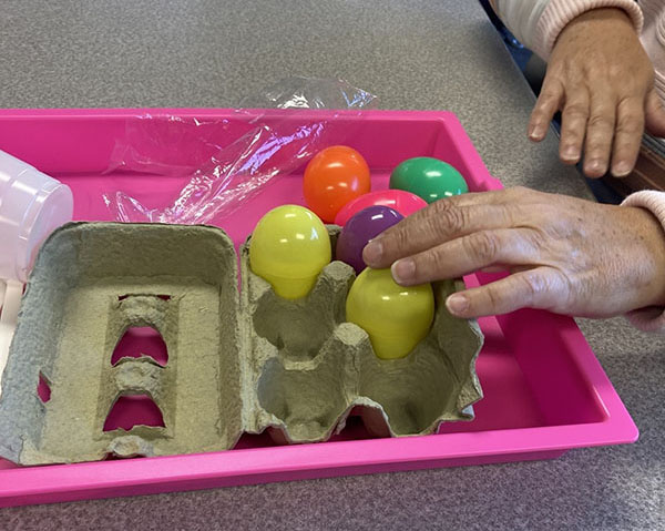 A woman's hand reaching to grab a colorful plastic egg from an egg carton.