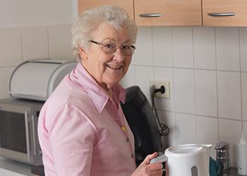 older woman holding a coffeepot in a kitchen